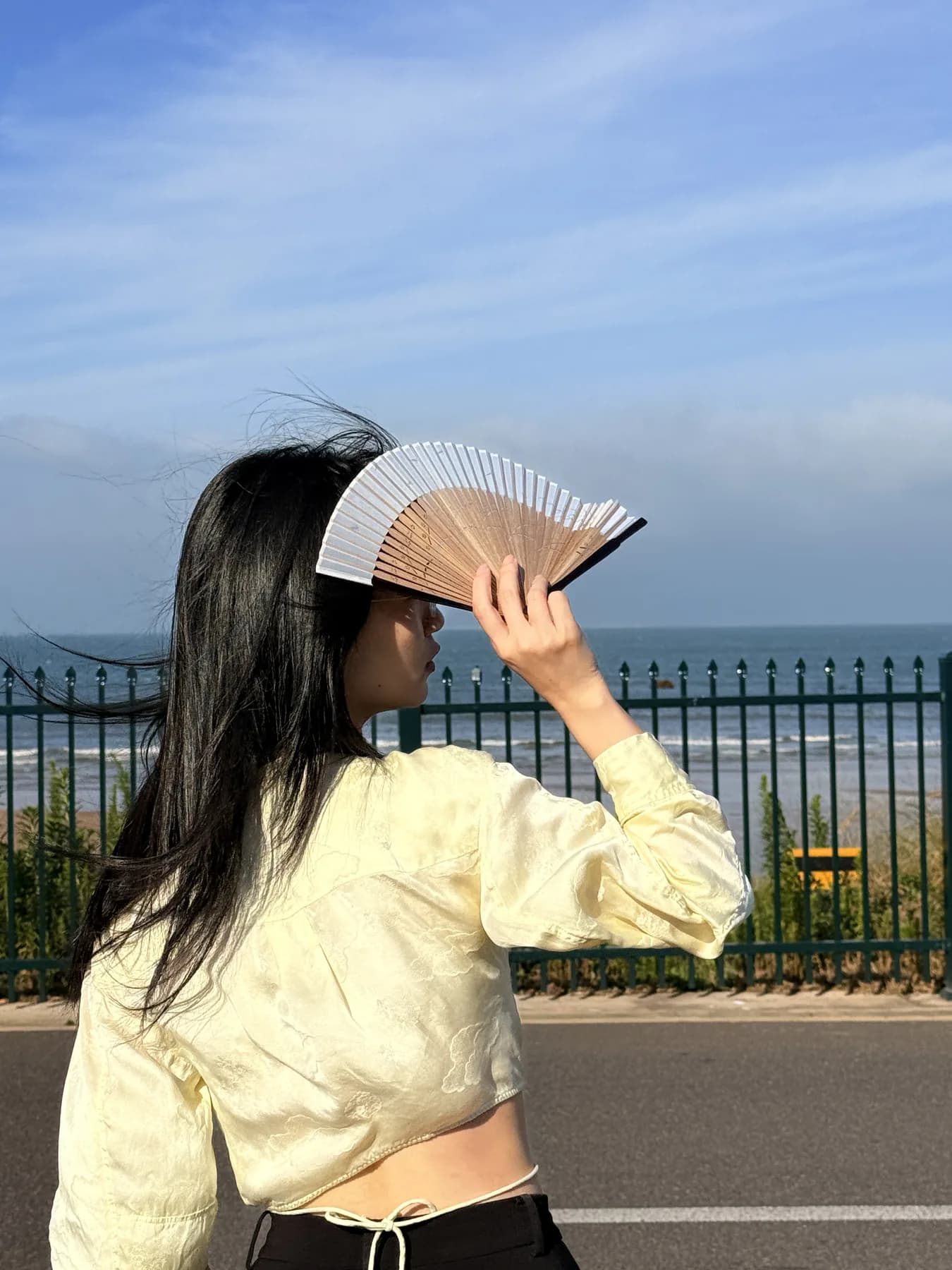青岛海边的栏杆旁,Aria 举着一把折扇遮阳